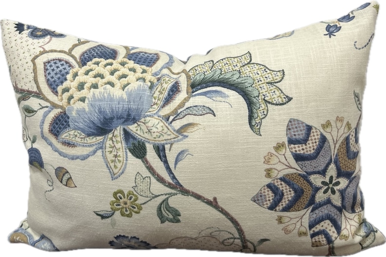 Puede incluir: Una almohada decorativa con un patr&oacute;n floral en tonos azules, verdes y marrones sobre un fondo crema.