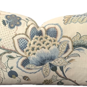 Puede incluir: Una almohada decorativa con un patr&oacute;n floral en tonos azules, verdes y marrones sobre un fondo crema.