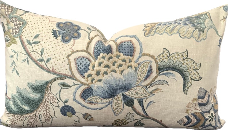 Puede incluir: Una almohada decorativa con un patr&oacute;n floral en tonos azules, verdes y marrones sobre un fondo crema.