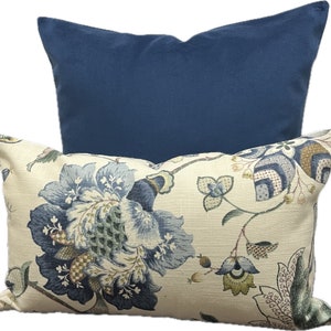 Puede incluir: Dos almohadas decorativas, una con un patr&oacute;n floral en tonos azules, verdes y crema sobre un fondo crema, y la otra azul s&oacute;lido.