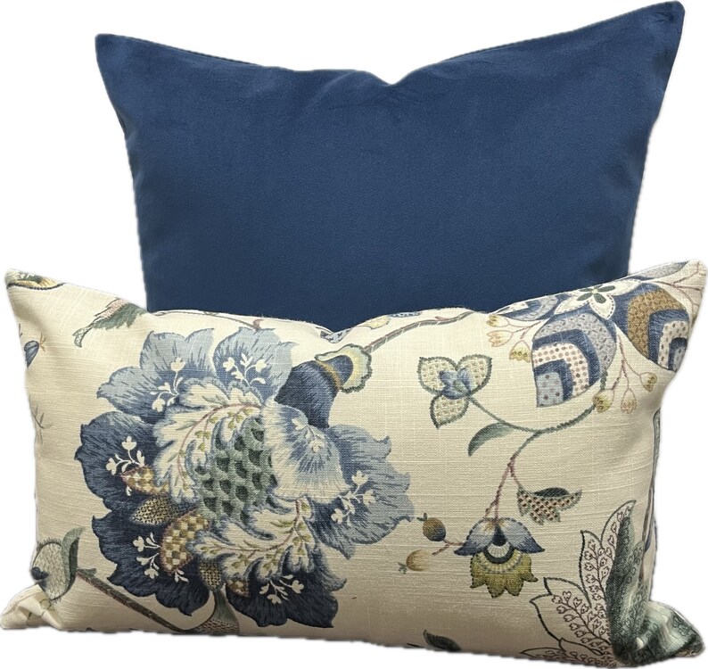 Puede incluir: Dos almohadas decorativas, una con un patr&oacute;n floral en tonos azules, verdes y crema sobre un fondo crema, y la otra azul s&oacute;lido.