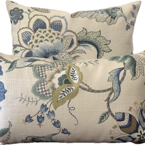 Puede incluir: Dos almohadas decorativas con un patr&oacute;n floral en tonos azules, verdes y marrones sobre un fondo crema.