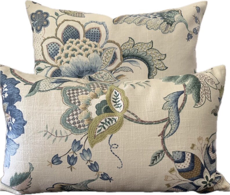 Puede incluir: Dos almohadas decorativas con un patr&oacute;n floral en tonos azules, verdes y marrones sobre un fondo crema.