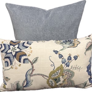 Puede incluir: Dos almohadas decorativas, una con un patr&oacute;n floral en tonos azules, verdes y marrones sobre un fondo crema, y la otra de color azul claro s&oacute;lido.