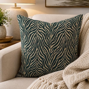 May include: A square throw pillow featuring a dark teal and beige zebra stripe pattern. The fabric has a visible woven texture, and the design consists of vertical, repeating animal print lines that cover the entire front surface of the pillow.