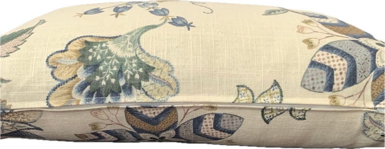 Puede incluir: Una almohada beige con un patr&oacute;n floral en tonos azules, verdes y marrones. La almohada tiene una cremallera.