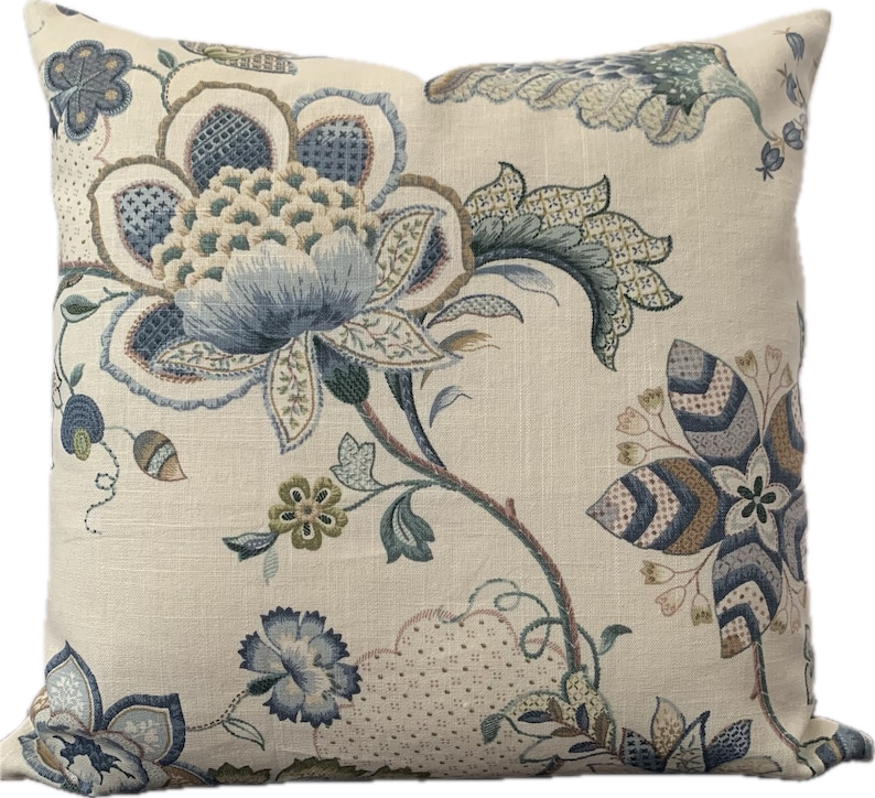Puede incluir: Una almohada decorativa con un patr&oacute;n floral en tonos azules, verdes y marrones sobre un fondo crema.