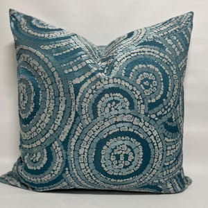 May include: Teal blue throw pillow with a white and teal circular pattern.