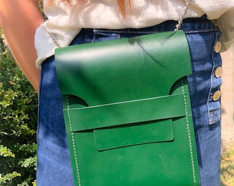 Könnte beinhalten: Eine kleine grüne Ledertasche mit einem silbernen Kettenriemen. Die Tasche hat einen Klappverschluss und ein kleines Fach auf der Vorderseite.