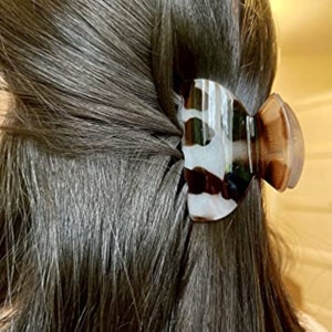May include: A brown and white patterned hair claw clip. The claw clip is made of plastic and has a smooth, glossy finish.