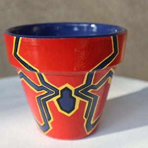May include: Red terracotta flower pot with a blue and yellow spider-man design.