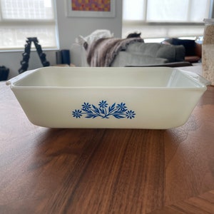 Może przedstawiać: Biała ceramiczna forma do chleba z niebieskim wzorem kwiatowym. Forma znajduje się na drewnianej powierzchni.