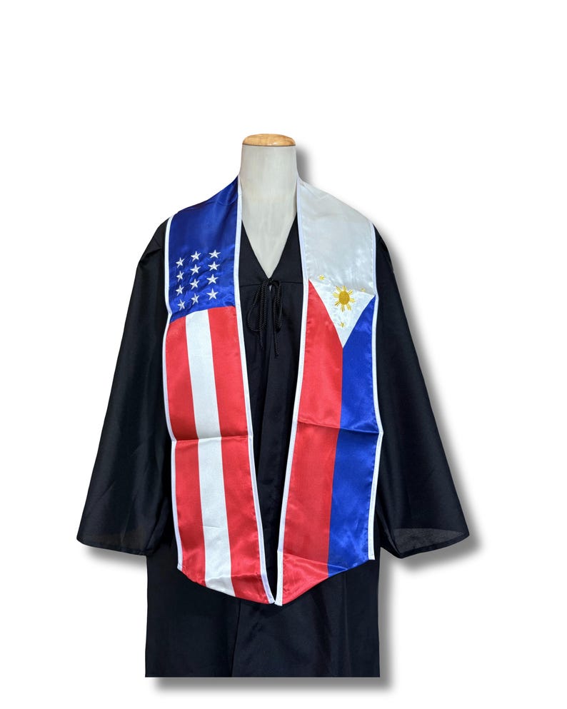 May include: A graduation sash with the American and Philippine flags printed on it. The sash is white with red and blue stripes.