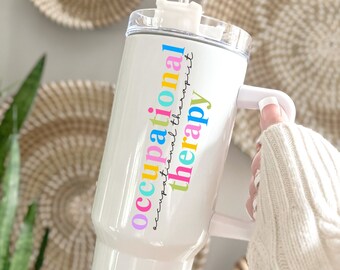 May include: White stainless steel travel mug with a pink, yellow, blue, and green design that says "occupational therapy". The mug has a lid with a straw and a handle.