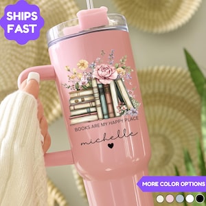 May include: A pink insulated tumbler with a handle, featuring a floral and book design. The text "BOOKS ARE MY HAPPY PLACE" and a name are printed on the tumbler. Includes a straw and lid.