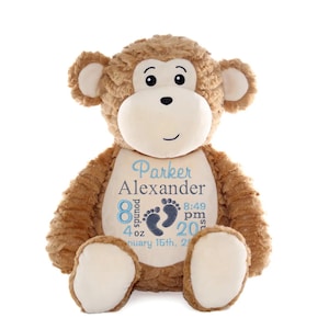 May include: A plush monkey with brown fur, a cream-colored face, and large ears. The monkey has embroidered details, including a name, weight (8 pounds 4 ounces), time, and date in blue. The monkey is designed to be a baby keepsake.