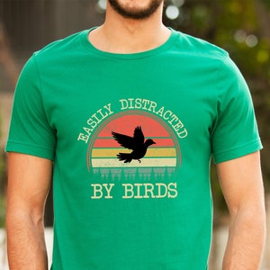 May include: A green t-shirt with a retro sunset graphic and the text "Easily Distracted By Birds".