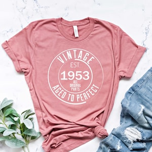 May include: A pink t-shirt with a white circle graphic that says "Vintage Est. 1953 All Original Parts Aged to Perfect".