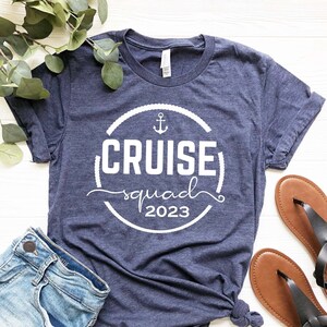 May include: A navy blue t-shirt with a white circle design that says "Cruise squad 2023" with an anchor symbol inside the circle.