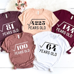 May include: Five t-shirts with different designs featuring the square root of a number followed by the text "YEARS OLD". The shirts are in various colors, including maroon, beige, white, and burgundy.