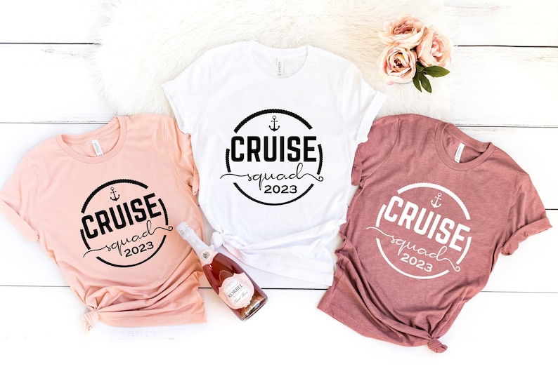 May include: Three t-shirts with a black and white graphic design that says "(CRUISE) squad 2023" with an anchor symbol. The shirts are in different colors: peach, white, and maroon.
