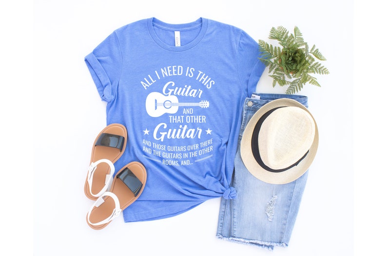 Puede incluir: Una camiseta azul con texto blanco que dice "All I need is this Guitar and that other Guitar and those guitars over there and the guitars in the other rooms, and..." con un contorno blanco de una guitarra ac&uacute;stica.