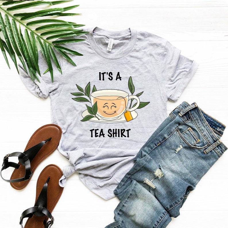 May include: A gray t-shirt with the text "It's a Tea Shirt" and a cartoon image of a smiling teacup with a tea bag.