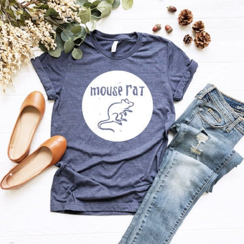 May include: A navy blue t-shirt with a white circle graphic featuring a rat and the text "mouse rat". The shirt is laid out on a white surface with a pair of brown flats and blue jeans.
