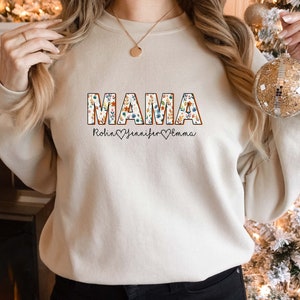 May include: A cream-colored sweatshirt with the word "MAMA" in floral letters. The names Robin, Jennifer, and Emma are written below the word "MAMA" with a heart symbol between each name.