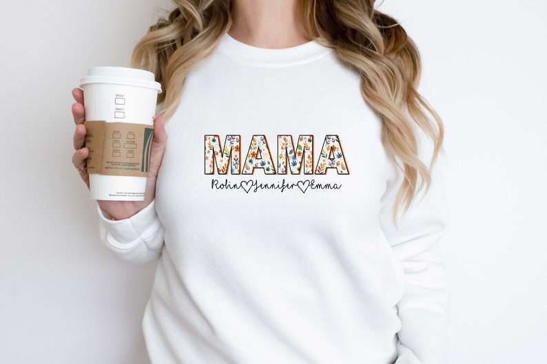 May include: White sweatshirt with the word "MAMA" in floral patterned letters. Below the word "MAMA" are the names "Robin", "Jennifer", and "Emma" with hearts between each name.