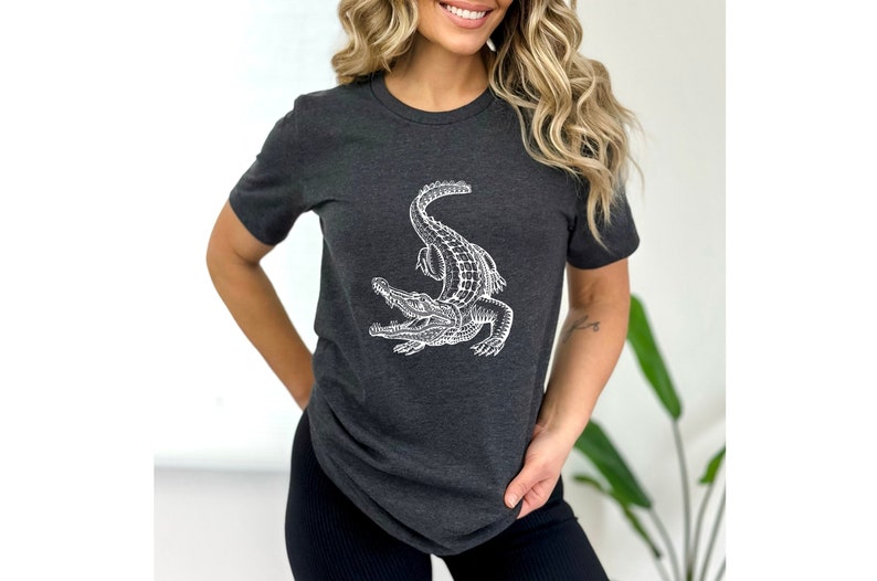 Puede incluir: Una camiseta gris oscuro con un gr&aacute;fico blanco de un caim&aacute;n. El caim&aacute;n est&aacute; mirando hacia el lado derecho de la imagen y tiene la boca abierta.