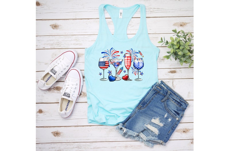 Pode incluir: Um top sem mangas azul claro com um gr&aacute;fico de quatro copos com designs de bandeira americana e fogos de artif&iacute;cio. Os copos est&atilde;o cheios de l&iacute;quidos vermelho, branco e azul. O top sem mangas &eacute; combinado com shorts jeans.