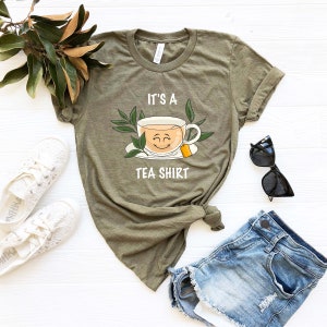 May include: A green t-shirt with the text "It's a Tea Shirt" and a cartoon image of a smiling teacup with a tea bag.