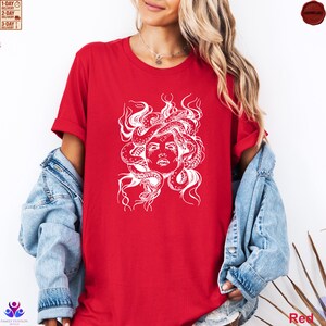 Pode incluir: Camiseta vermelha com um gr&aacute;fico branco do rosto de Medusa e cobras. O desenho est&aacute; centrado na camiseta. A modelo est&aacute; usando uma jaqueta jeans sobre a camiseta. A camiseta &eacute; de cor vermelha s&oacute;lida.