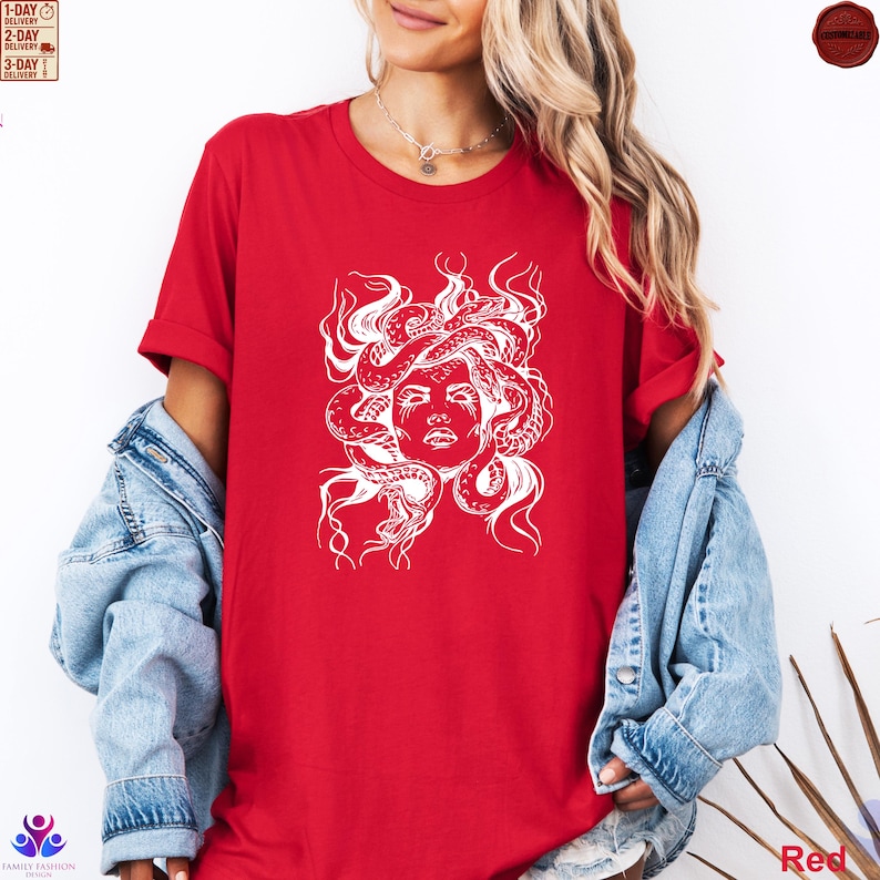 Pode incluir: Camiseta vermelha com um gr&aacute;fico branco do rosto de Medusa e cobras. O desenho est&aacute; centrado na camiseta. A modelo est&aacute; usando uma jaqueta jeans sobre a camiseta. A camiseta &eacute; de cor vermelha s&oacute;lida.