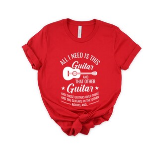 Puede incluir: Camiseta roja con un gr&aacute;fico blanco que dice "Todo lo que necesito es esta guitarra y esa otra guitarra y esas guitarras de all&aacute; y las guitarras en las otras habitaciones, y..."