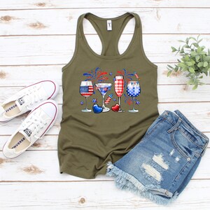Pode incluir: Uma camiseta sem mangas verde com um gr&aacute;fico de quatro copos de vinho decorados com cores vermelho, branco e azul, que lembram a bandeira portuguesa. Os copos s&atilde;o cercados por fogos de artif&iacute;cio vermelho, branco e azul.