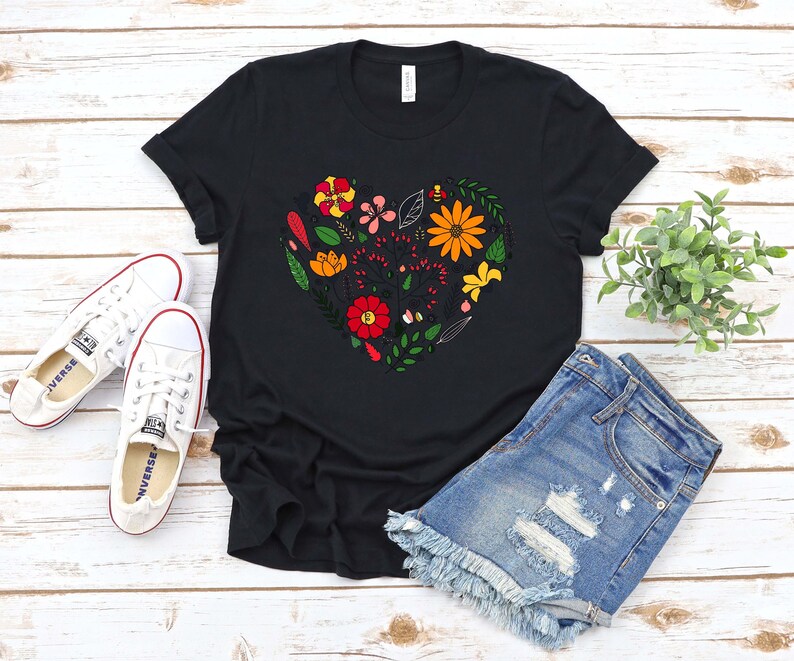 May include: Black t-shirt with a floral heart design featuring various colors including red, orange, yellow, and green. The design is centered on the shirt.