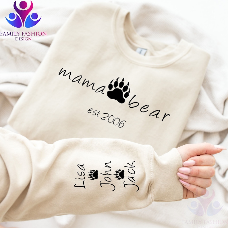 May include: A beige sweatshirt with the text "mama bear est. 2006" on the front and the names "Lisa", "John", and "Jack" with paw prints on the sleeve.