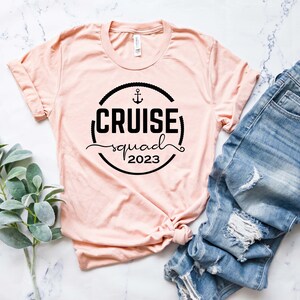 May include: A pink t-shirt with a black circle graphic that says "CRUISE squad 2023" with an anchor symbol above the text.