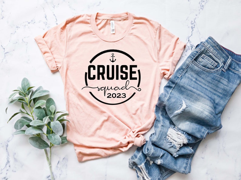May include: A pink t-shirt with a black circle graphic that says "CRUISE squad 2023" with an anchor symbol above the text.