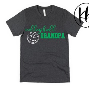 K&ouml;nnte beinhalten: Ein dunkelgraues T-Shirt mit dem Text "Volleyball Grandpa" in gr&uuml;ner und wei&szlig;er Schrift. Eine wei&szlig;e Volleyballgrafik befindet sich mittig &uuml;ber dem Text.