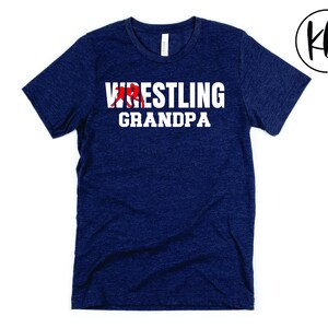 Puede incluir: Una camiseta azul marino con el texto "Wrestling Grandpa" en letras blancas. Se incluye una silueta roja de un luchador en el texto.