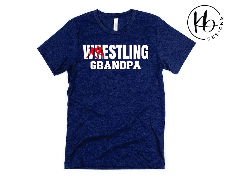 Puede incluir: Una camiseta azul marino con el texto "Wrestling Grandpa" en letras blancas. Se incluye una silueta roja de un luchador en el texto.