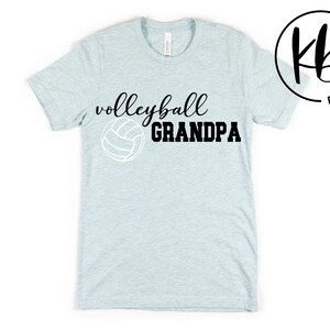 K&ouml;nnte beinhalten: Hellblaues T-Shirt mit schwarzem Text "Volleyball Grandpa" und einer wei&szlig;en Volleyballgrafik.
