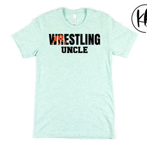 May include: A light blue t-shirt with the text "Wrestling Uncle" in black letters. The word "Wrestling" has a red and black wrestler graphic.