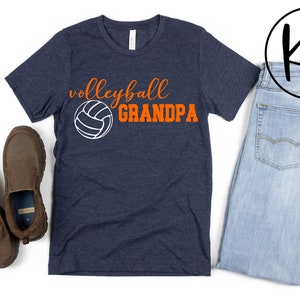 K&ouml;nnte beinhalten: Ein marineblaues T-Shirt mit dem Text "volleyball GRANDPA" in orangefarbener und wei&szlig;er Schrift. Neben dem Text befindet sich eine wei&szlig;e Volleyballgrafik.