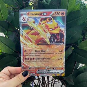 May include: A Pokemon trading card featuring Charizard EX, a fire-type Pokemon with orange and yellow flames. The card has a HP of 330 and features two attacks: Brave Wing and Explosive Vortex. The card is from the XY series.