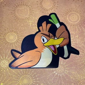 May include: A cartoon illustration of a brown and orange bird with a green stalk of celery in its beak. The bird has a black eye and a yellow beak. The background is black.