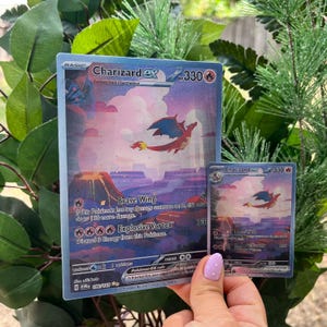 May include: Two Charizard EX Pokémon trading cards. The larger card features a red and blue dragon flying over a canyon landscape. The smaller card mirrors the design. Both cards have the number 330.